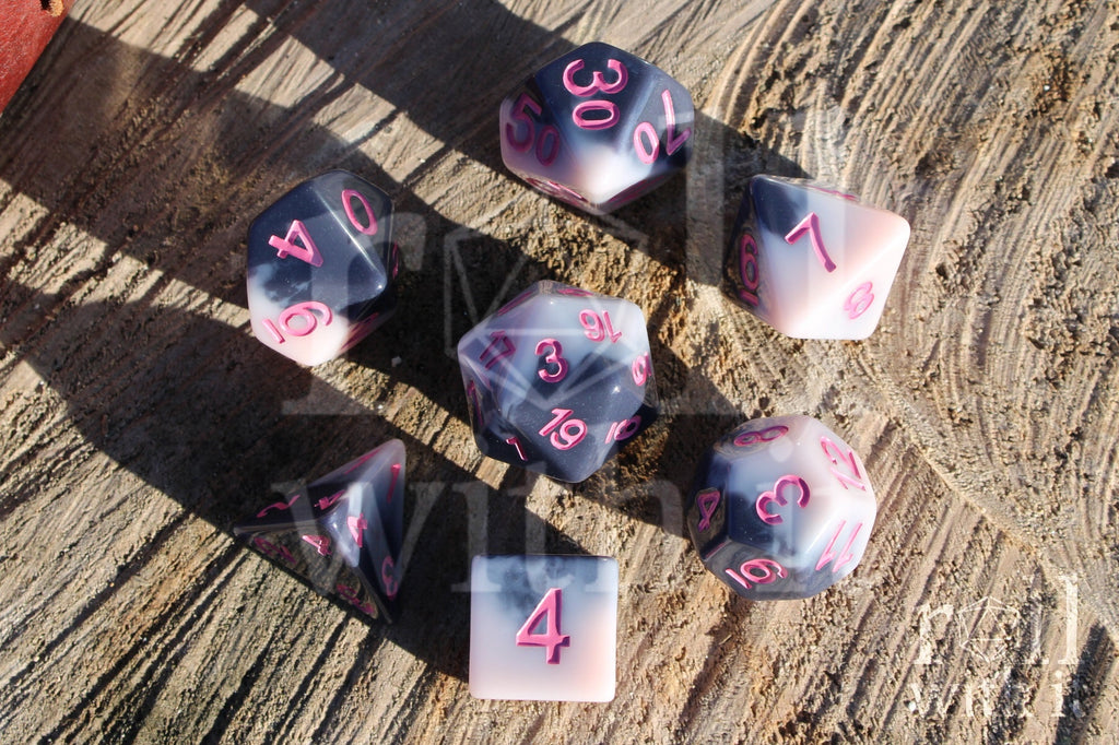 Set of pastel pink and grey polyhedral roleplaying dice with pink numbers sat on a wooden surface