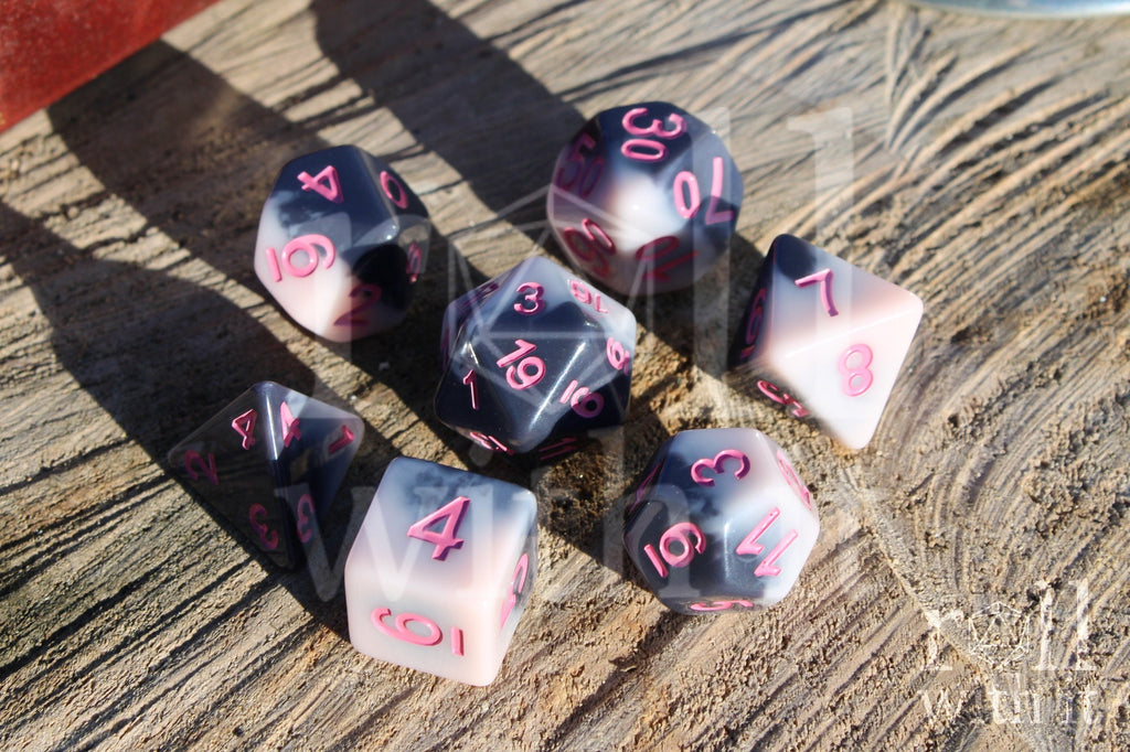 Set of pastel pink and grey polyhedral roleplaying dice with pink numbers sat on a wooden surface