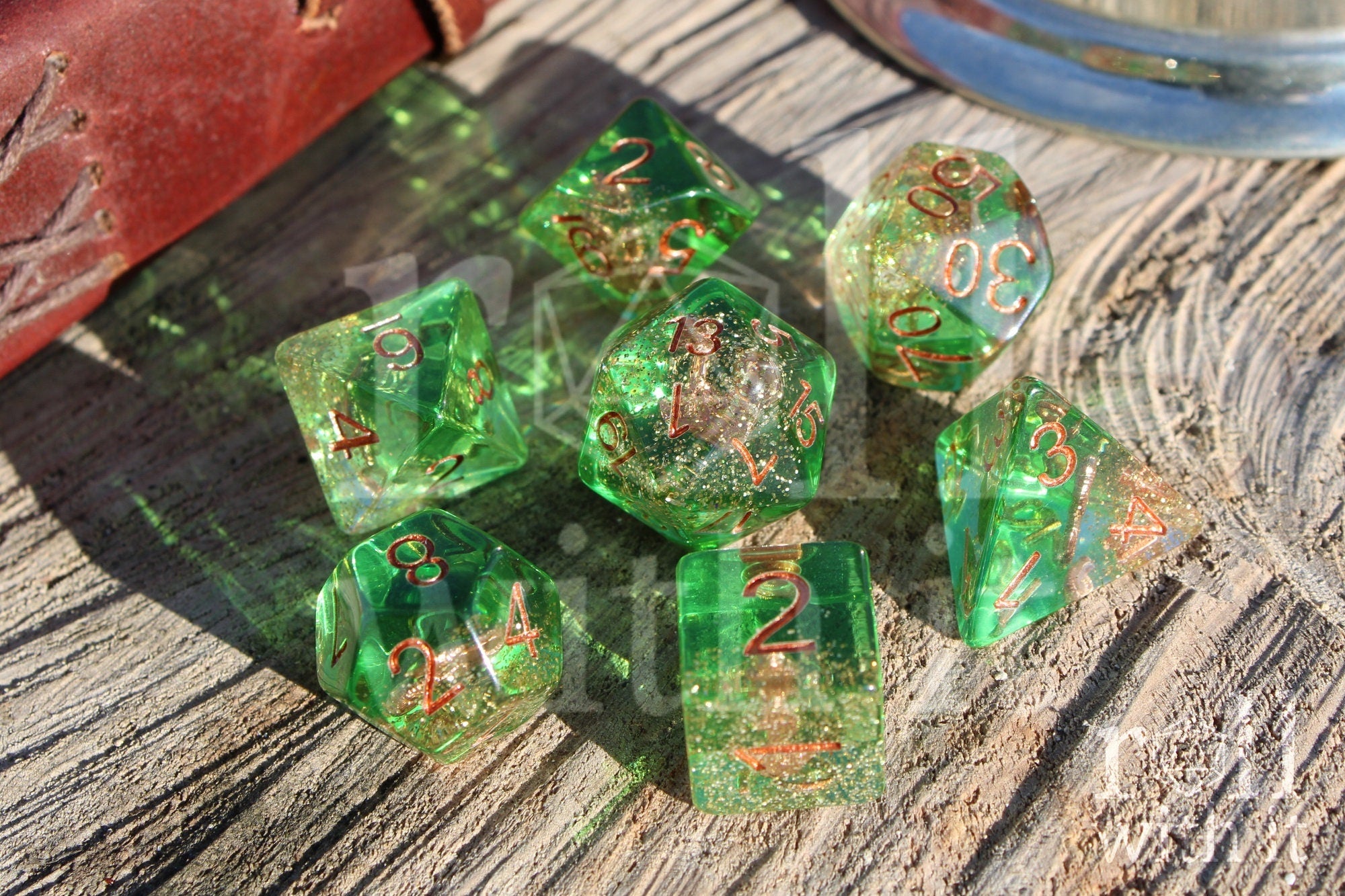 Set of green golden glittery dice with an anchor inside polyhedral dice with copper numbers on a wooden surface