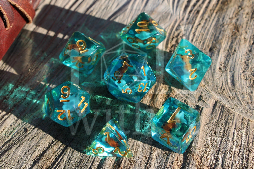 Set of clear blue turquoise polyhedral dice with gold numbers and a mini goldfish inside on a wooden surface