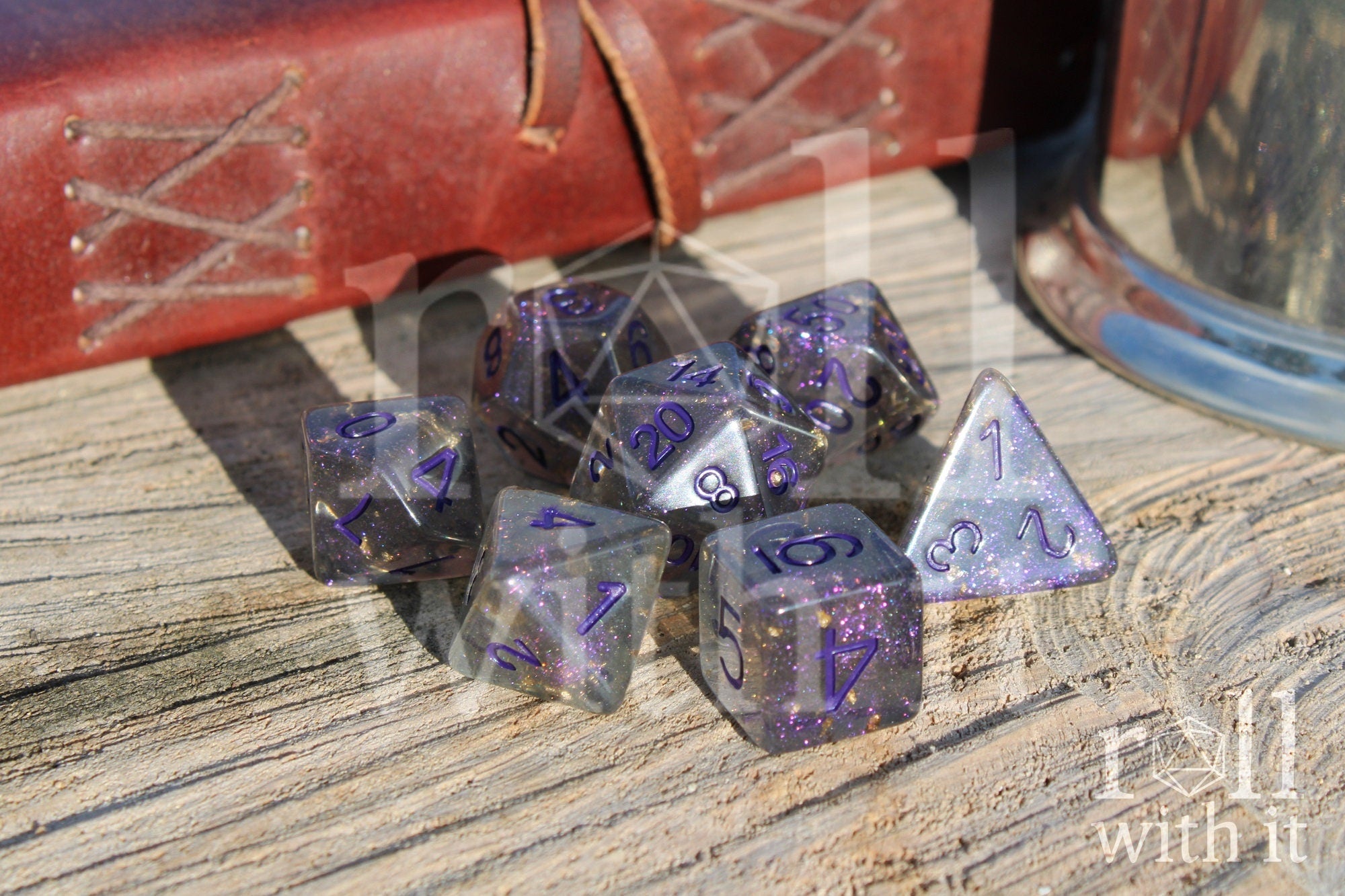 Set of grey shimmering and star like polyhedral dice with gold foil and purple numbers on a wooden background