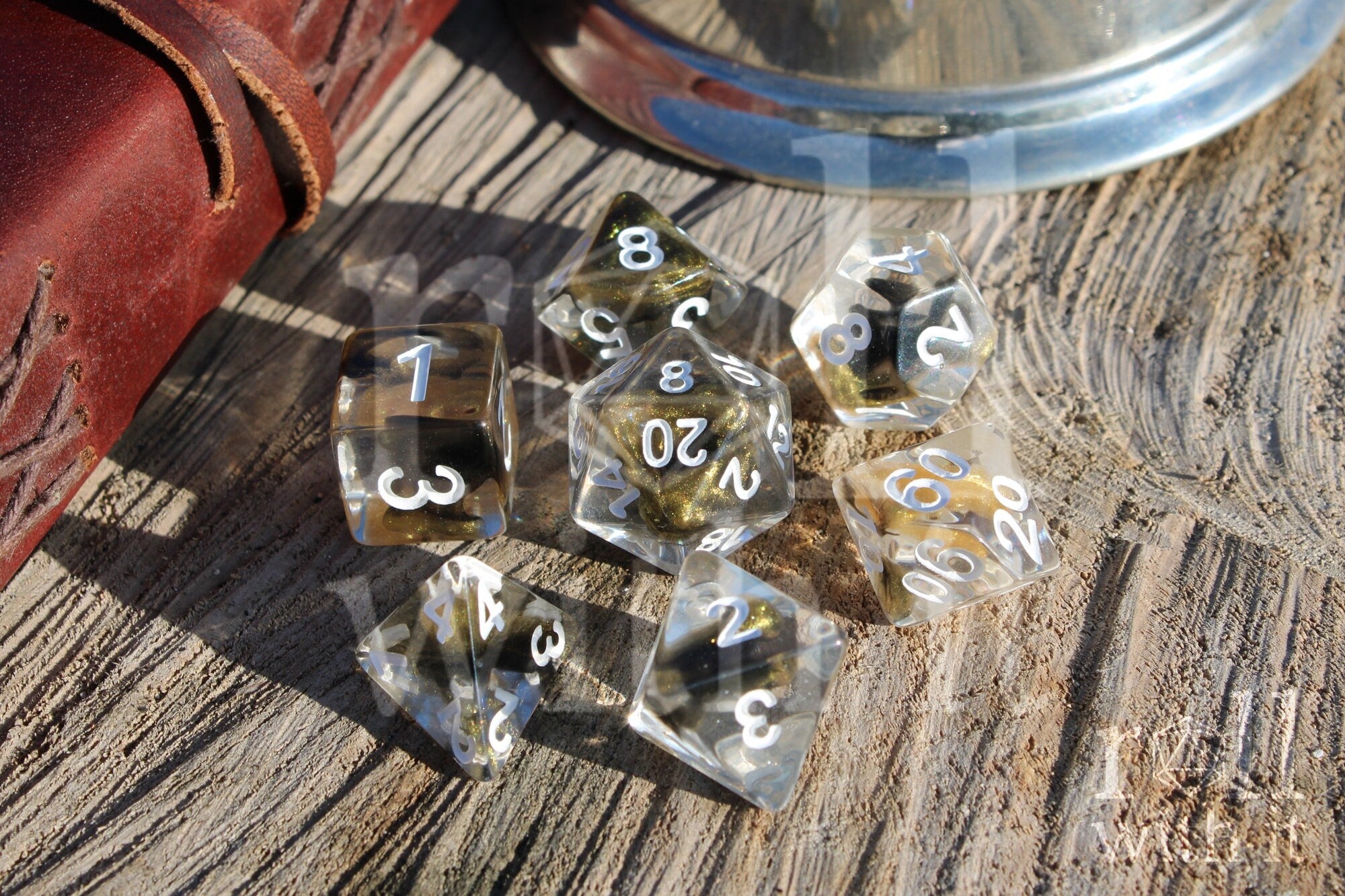 Set of clear polyhedral DND dice with gold and black glittering centres, with white numbers on a wooden surface