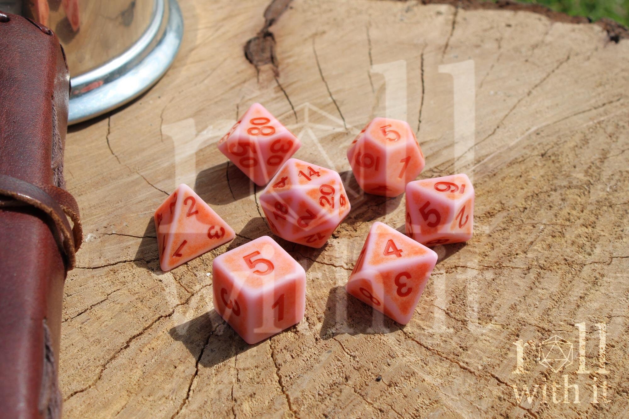 Set of matte pink polyhedral dice with red numbers on a wooden surface