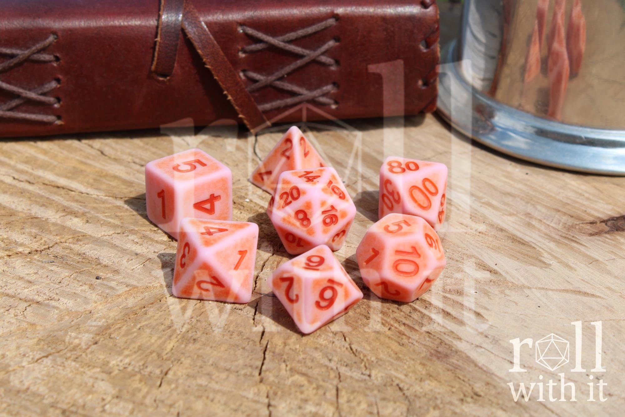Set of matte pink polyhedral dice with red numbers on a wooden surface