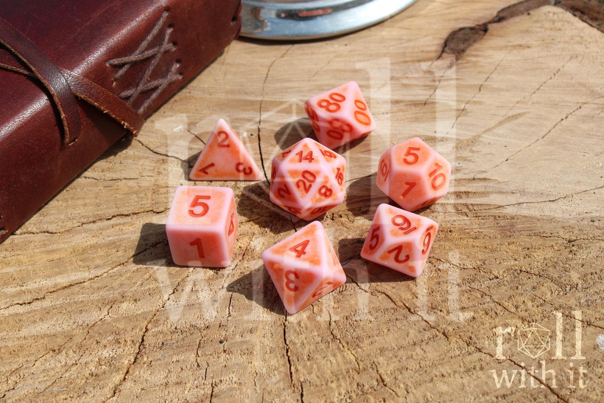 Set of matte pink polyhedral dice with red numbers on a wooden surface