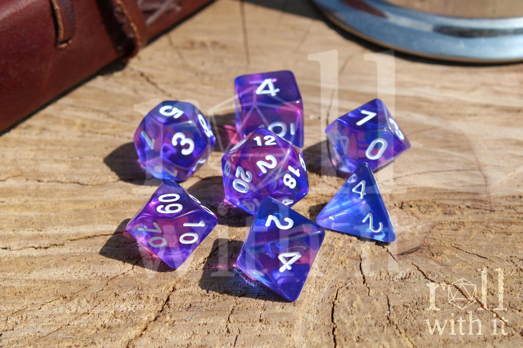 Set of clear blue and indigo purple polyhedral DND dice with white numbers on a wooden surface