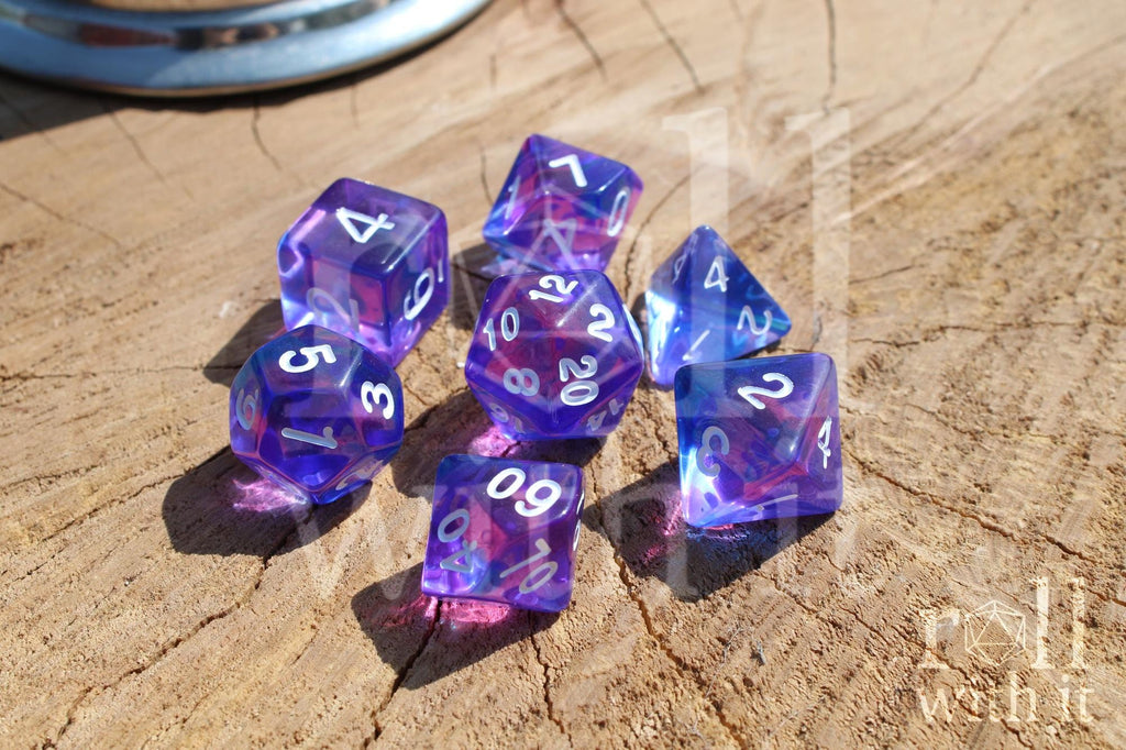 Set of clear blue and indigo purple polyhedral DND dice with white numbers on a wooden surface