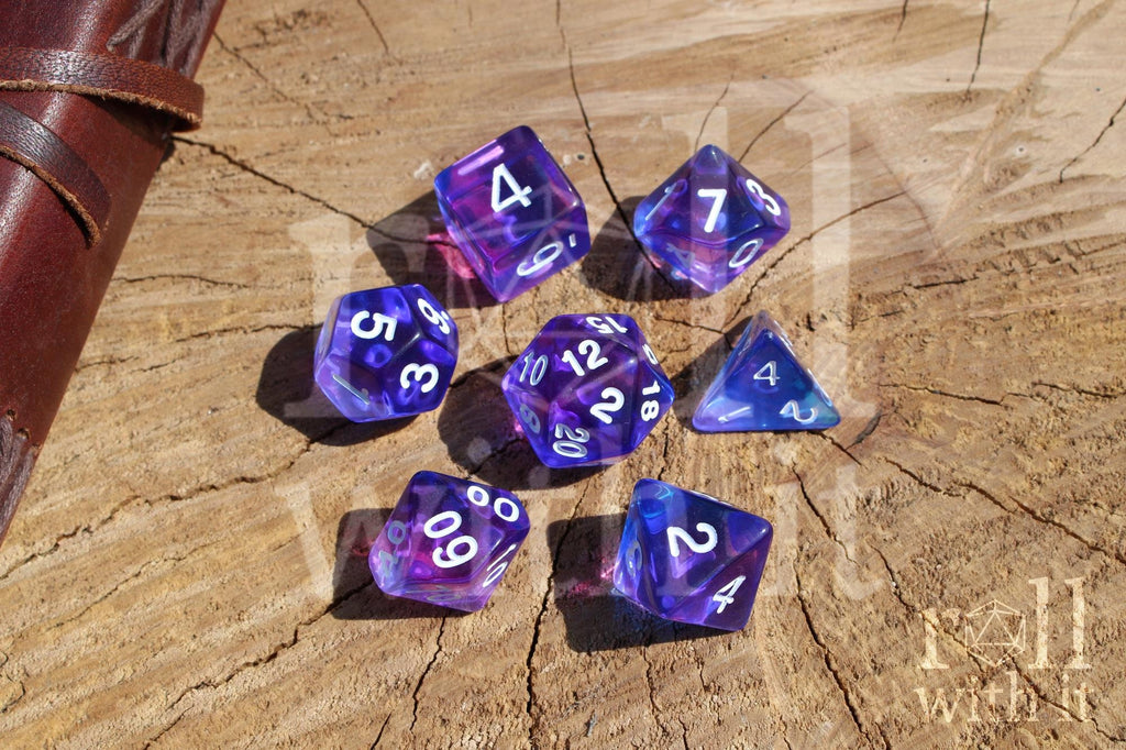 Set of clear blue and indigo purple polyhedral DND dice with white numbers on a wooden surface