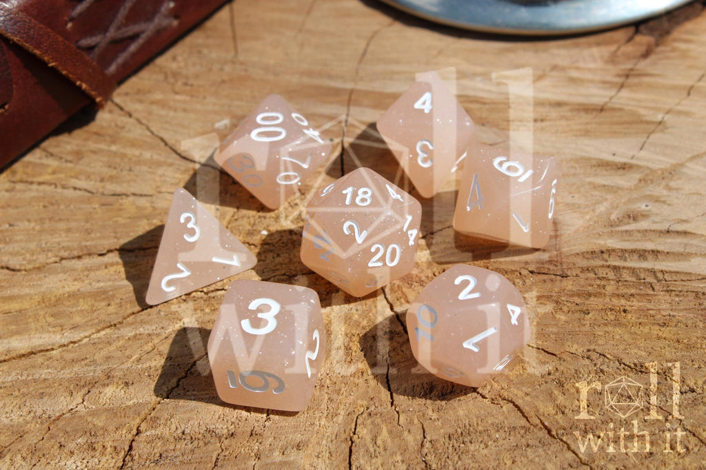 Set of creamy beige glittery polyhedral dice with white numbers on a wooden surface
