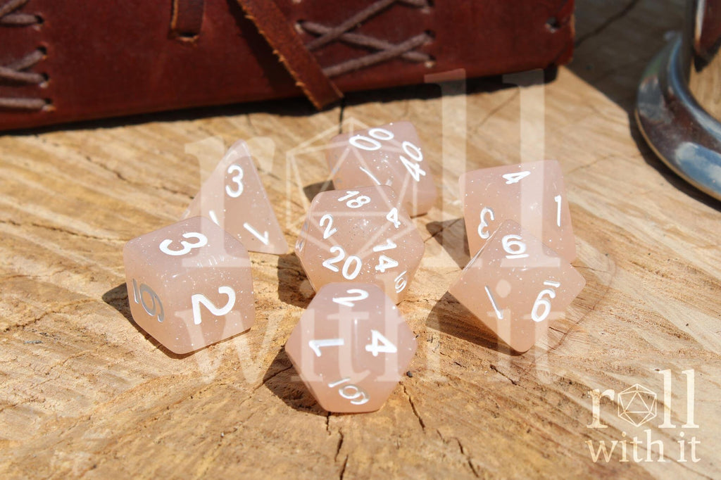 Set of creamy beige glittery polyhedral dice with white numbers on a wooden surface