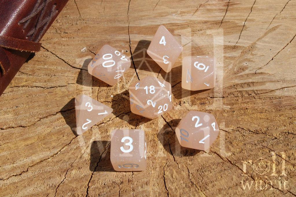 Set of creamy beige glittery polyhedral dice with white numbers on a wooden surface
