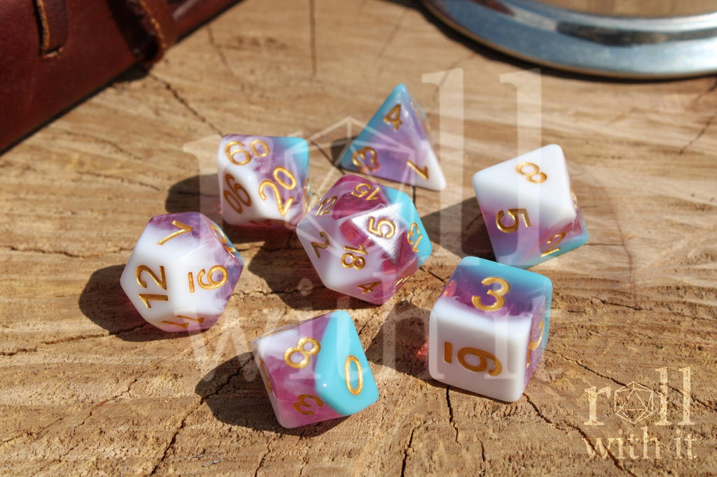 Set of colourful layered pink, light blue, and creamy white polyhedral DnD dice with gold numbers on a wooden surface