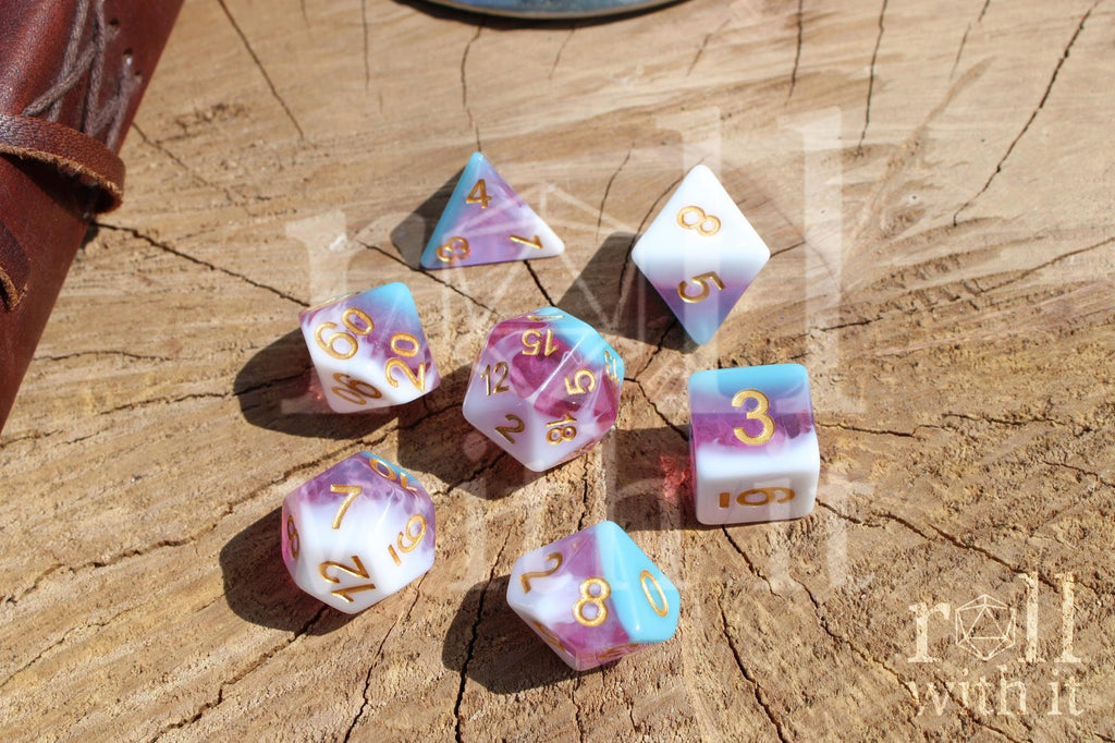 Set of colourful layered pink, light blue, and creamy white polyhedral role playing dice with gold numbers on a wooden surface