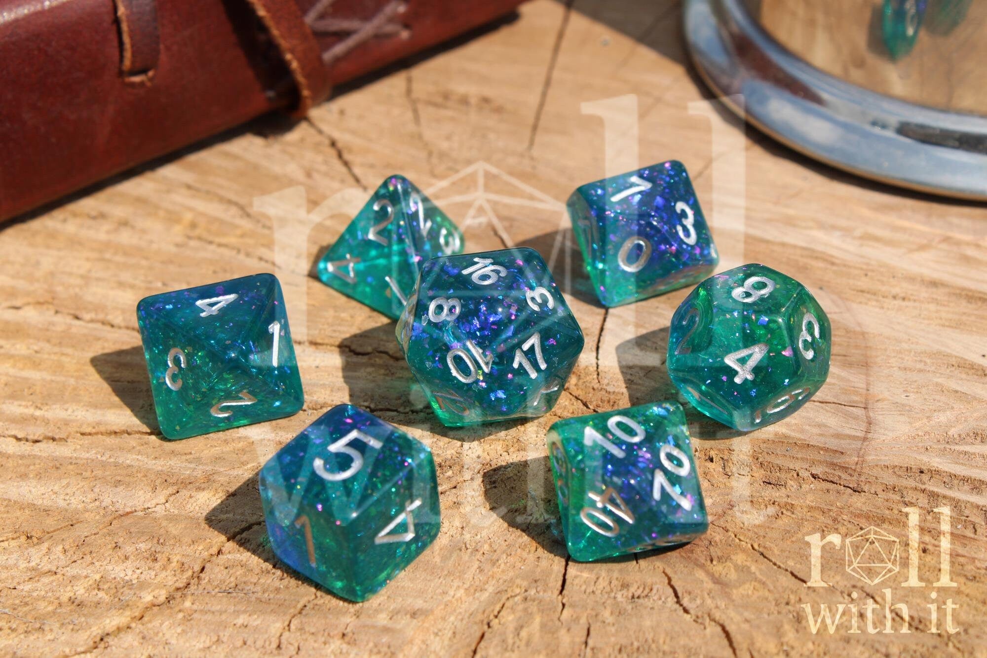 Set of 7 glittery and shining blue and green polyhedral DND dice with silver leaf inside on a wooden surface