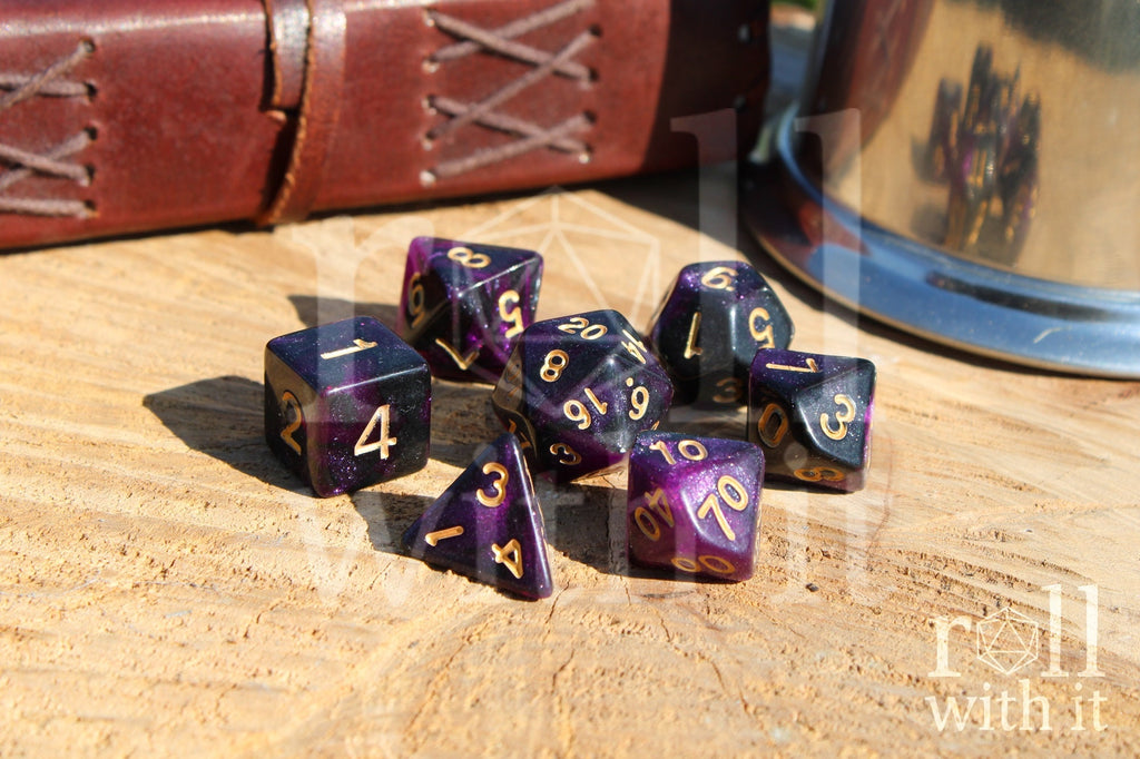 Purple and black glittery polyhedral dice set with gold numbers on a wooden surface