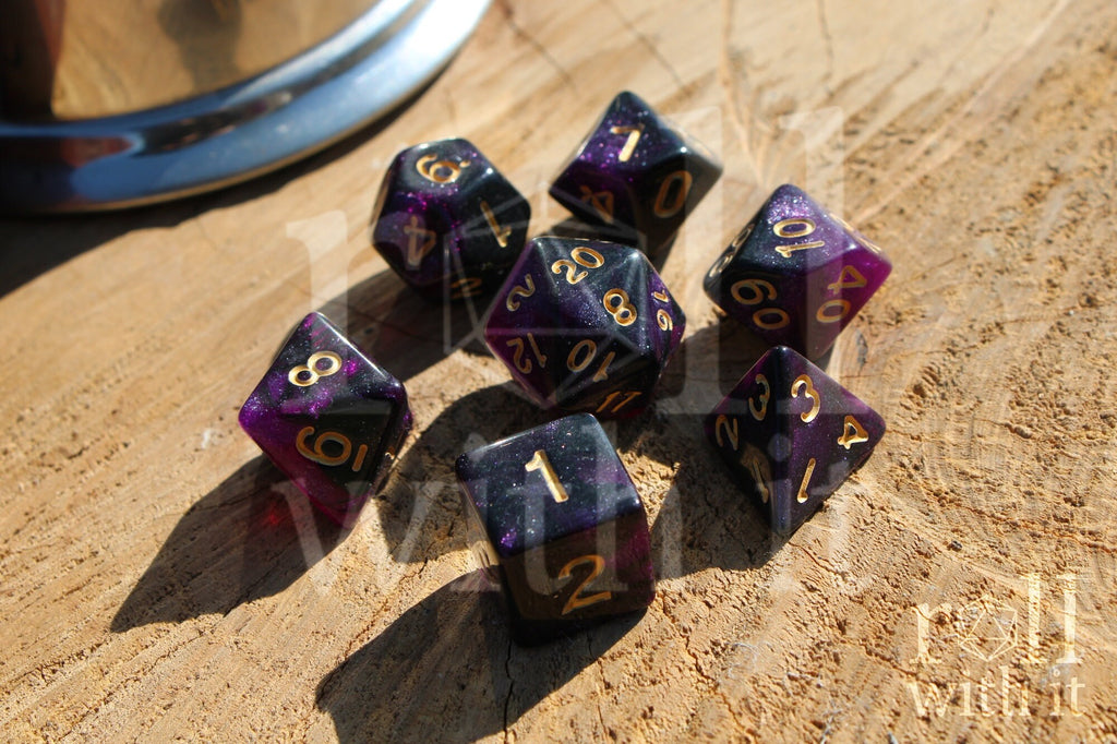 Purple and black glittery polyhedral dice set with gold numbers on a wooden surface