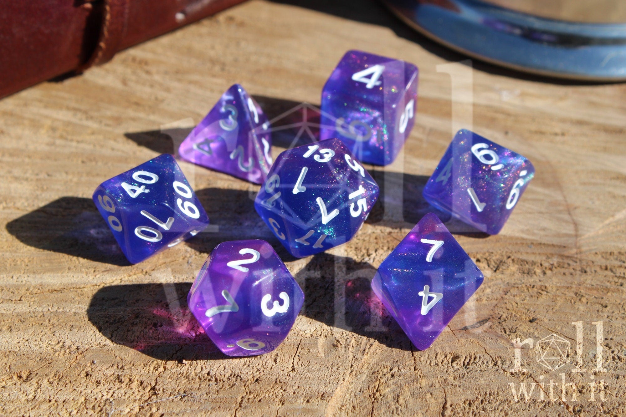 Set of glittery indigo purple polyhedral roleplaying dice with white numbers on a wooden surface