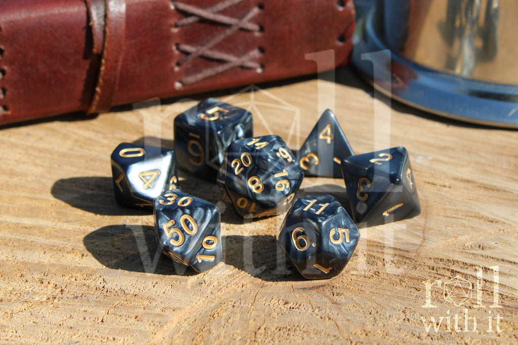 Set of black swirling polyhedral DnD dice with gold numbers on a wooden surface