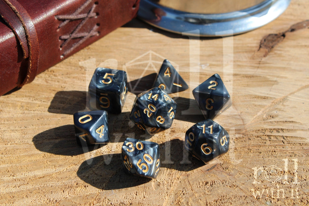 Set of black swirling polyhedral dice with gold numbers on a wooden surface
