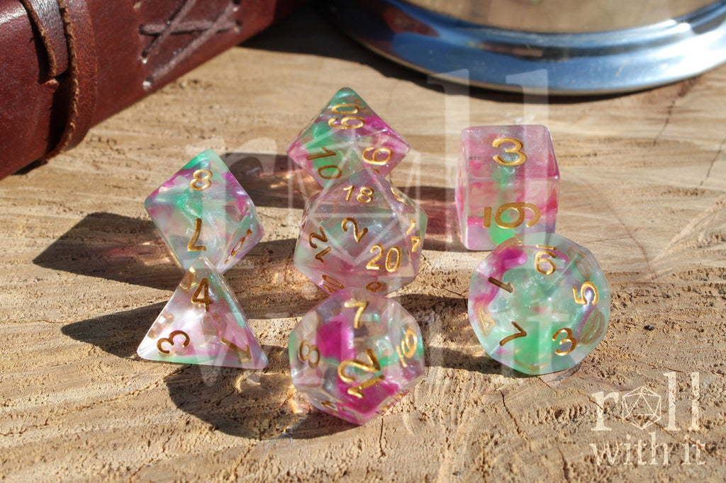 Set of fuschia pink and green clear polyhedral roleplaying dice with gold numbers on a wooden surface