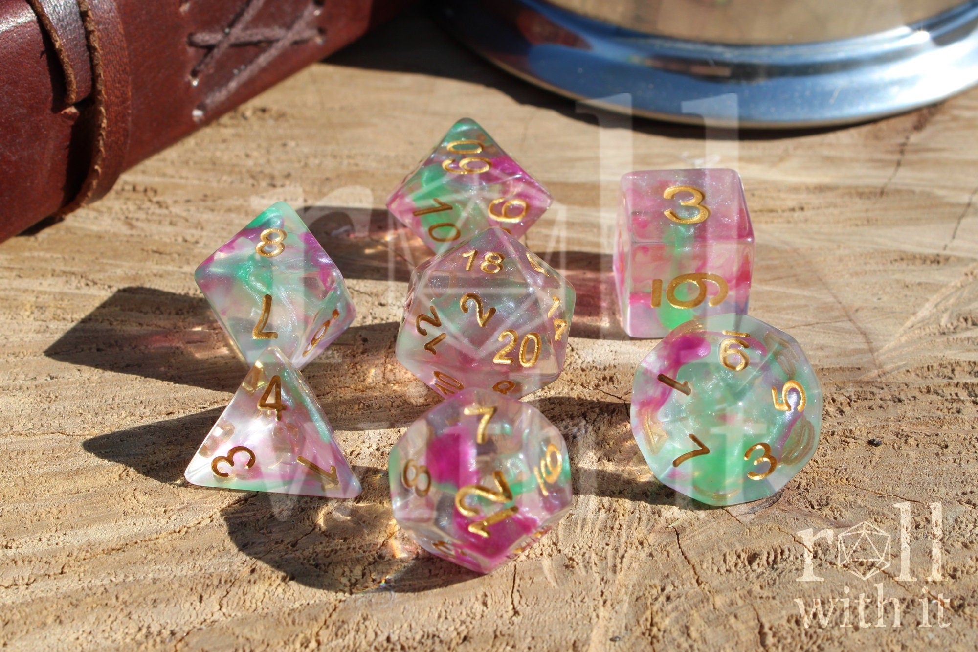 Set of fuschia pink and green clear polyhedral roleplaying dice with gold numbers on a wooden surface