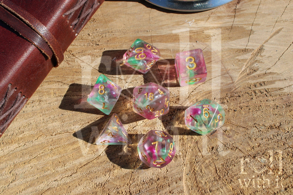 Set of fuschia pink and green clear roleplaying dice with gold numbers on a wooden surface