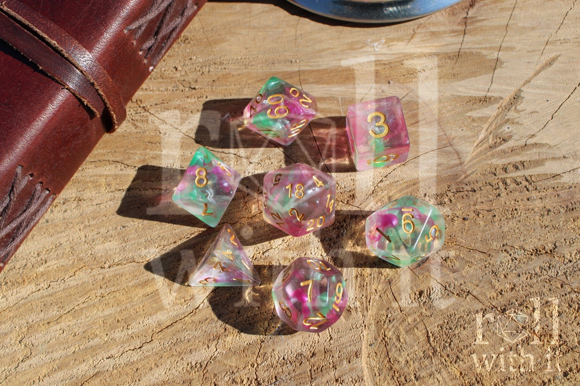 Set of fuschia pink and green clear roleplaying dice with gold numbers on a wooden surface
