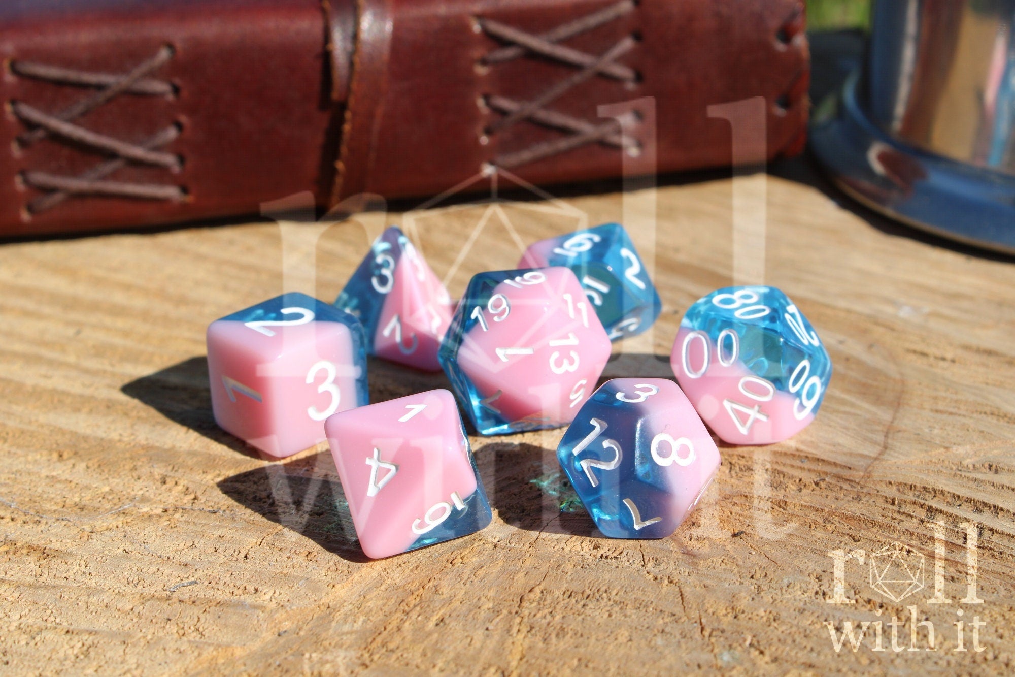 Set of bubblegum pink and clear blue polyhedral roleplaying dice on a wooden surface