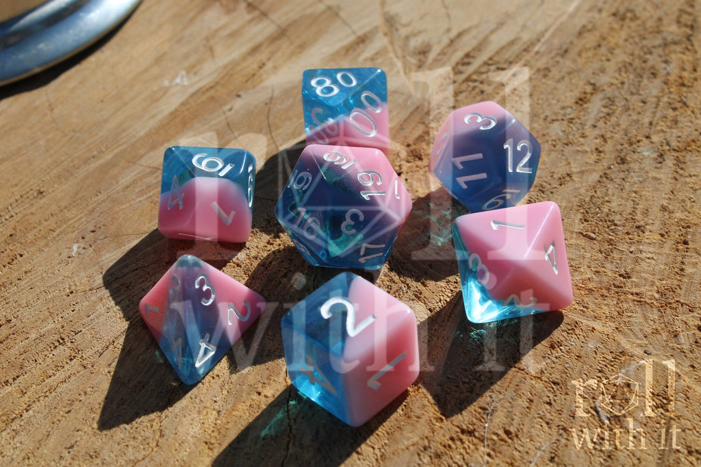 Set of bubblegum pink and clear blue polyhedral roleplaying dice on a wooden surface