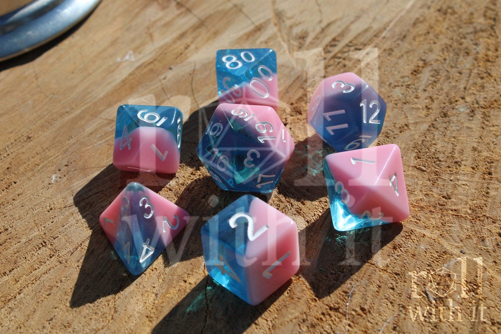 Set of bubblegum pink and clear blue polyhedral roleplaying dice on a wooden surface