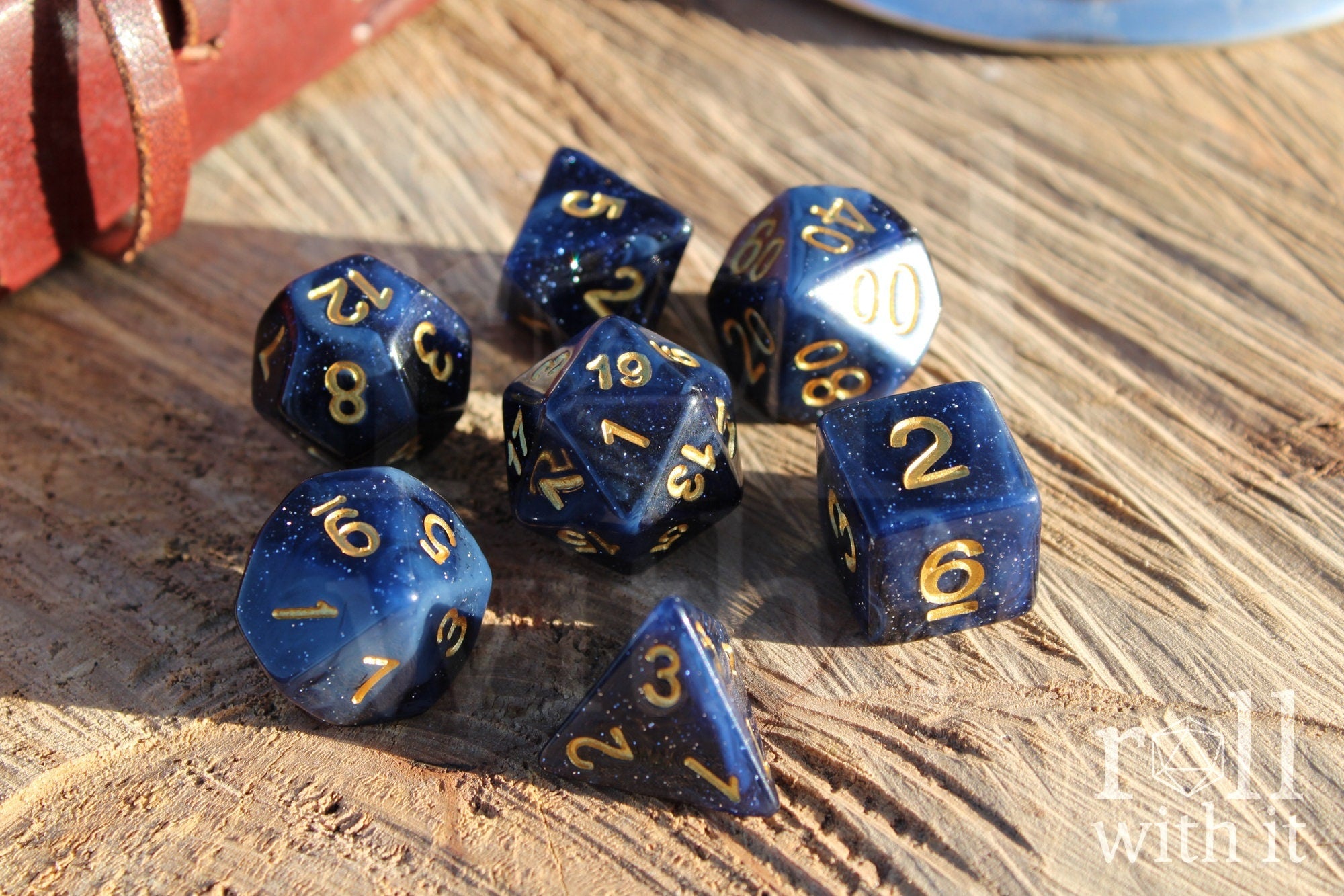 Deep midnight blue polyhedral starry glittery roleplaying dice with gold numbers on a wooden surface