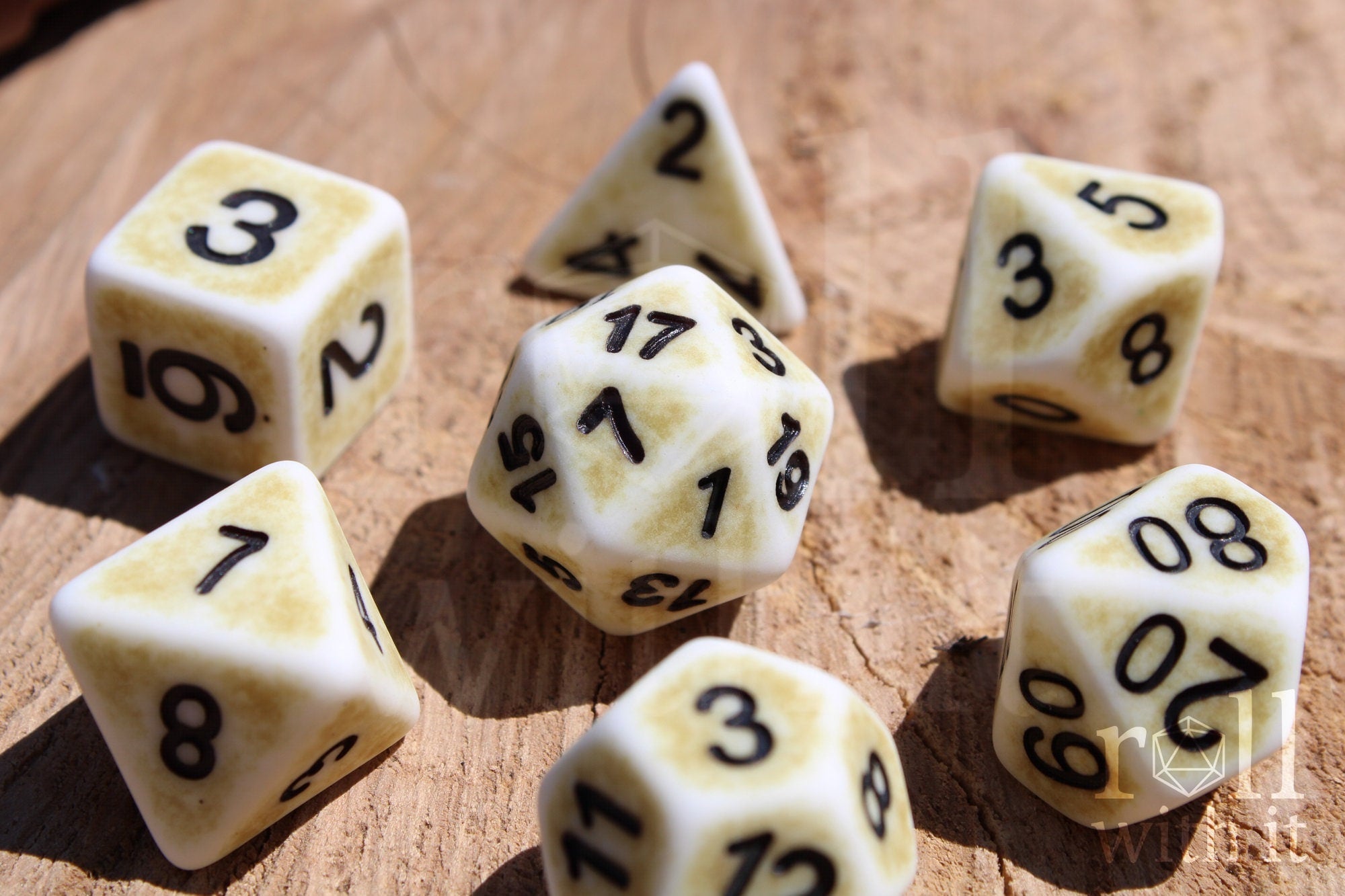 Set of creamy bone white matte roleplaying dice with a worn looking surface, with black numbers on a wooden surface