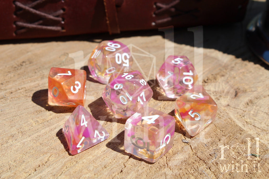 Set of colorful pink and orange clear polyhedral dice on a wooden surface