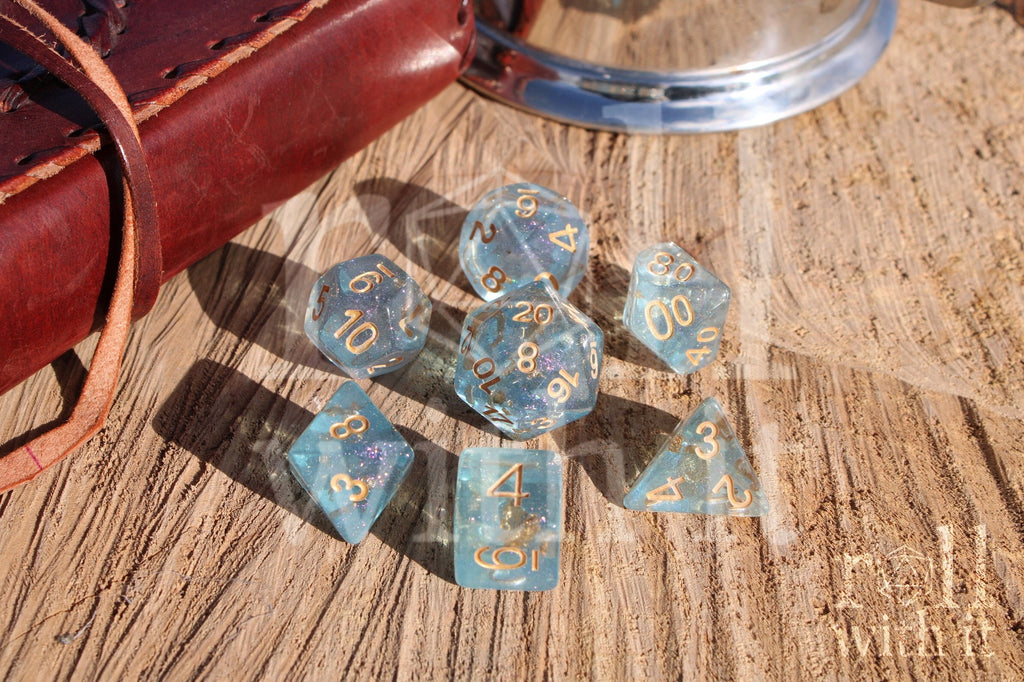 Set of clear blue and gold foil dice with gold numbers on a wooden surface