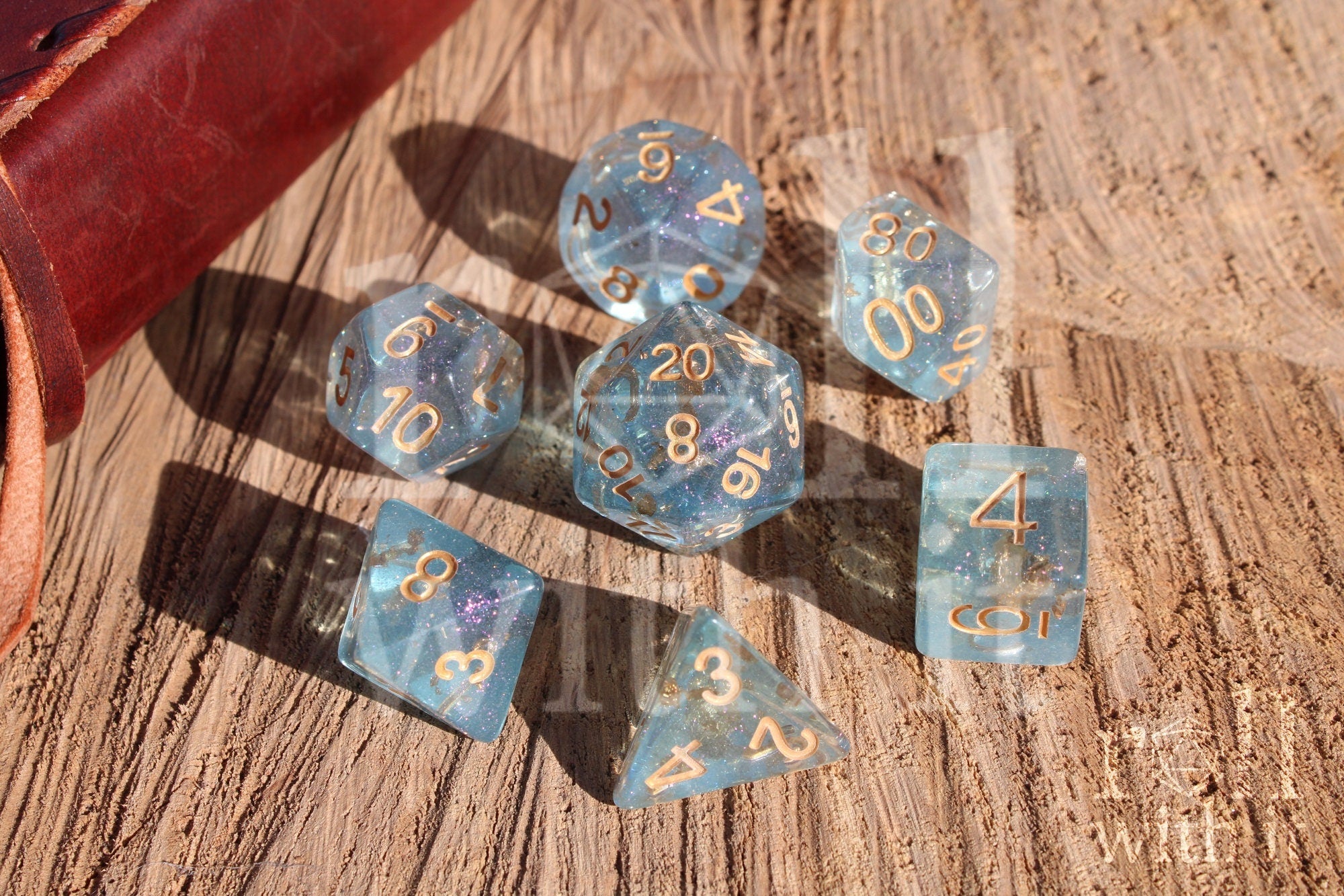 Set of clear blue and gold foil dice with gold numbers on a wooden surface