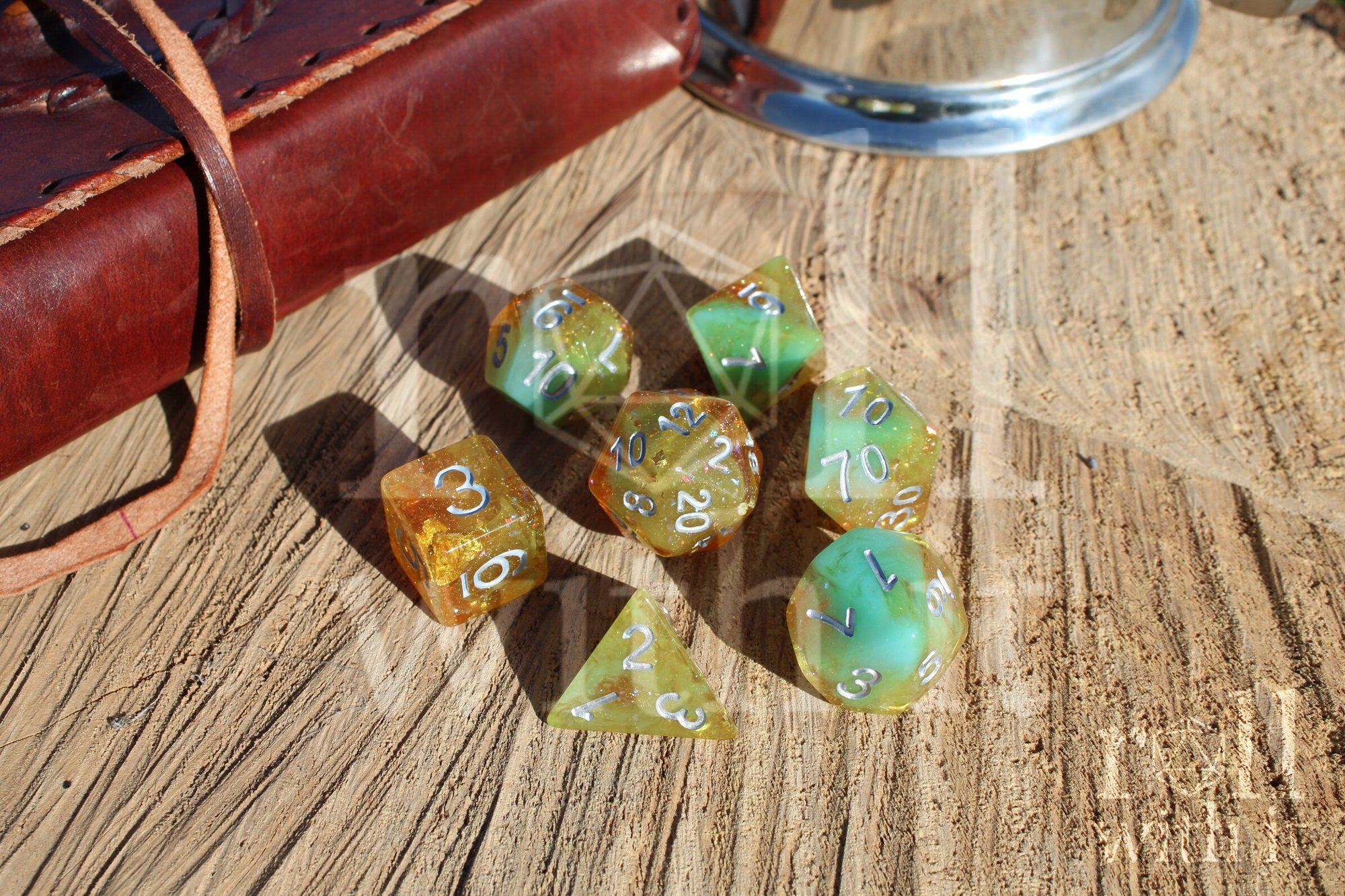 Set of colourful and glittery golden and teal polyhedral DND roleplaying dice with silver numbers on a wooden surface