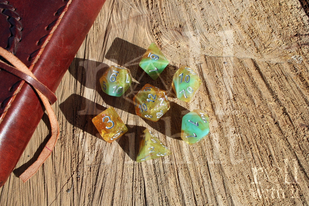 Set of colourful and glittery golden and teal polyhedral roleplaying DND dice with silver numbers on a wooden surface