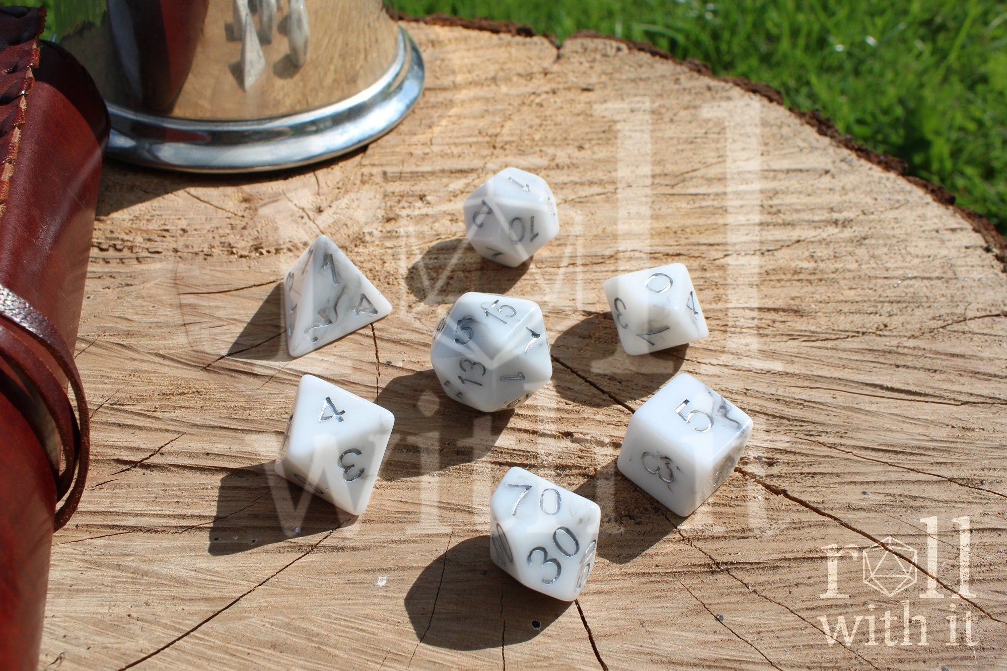 Granite white polyhedral DND dice with silver numbering on a wooden surface.