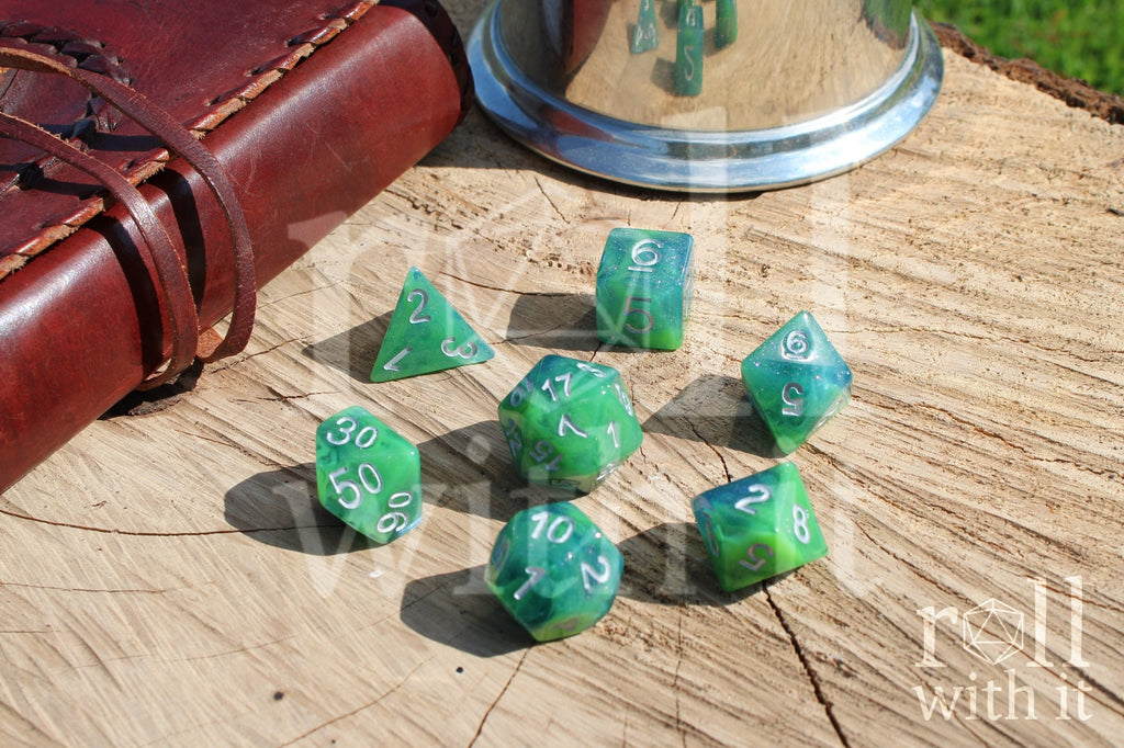 Set of green and blue glittery polyhedral dice with silver numbers on a wooden surface