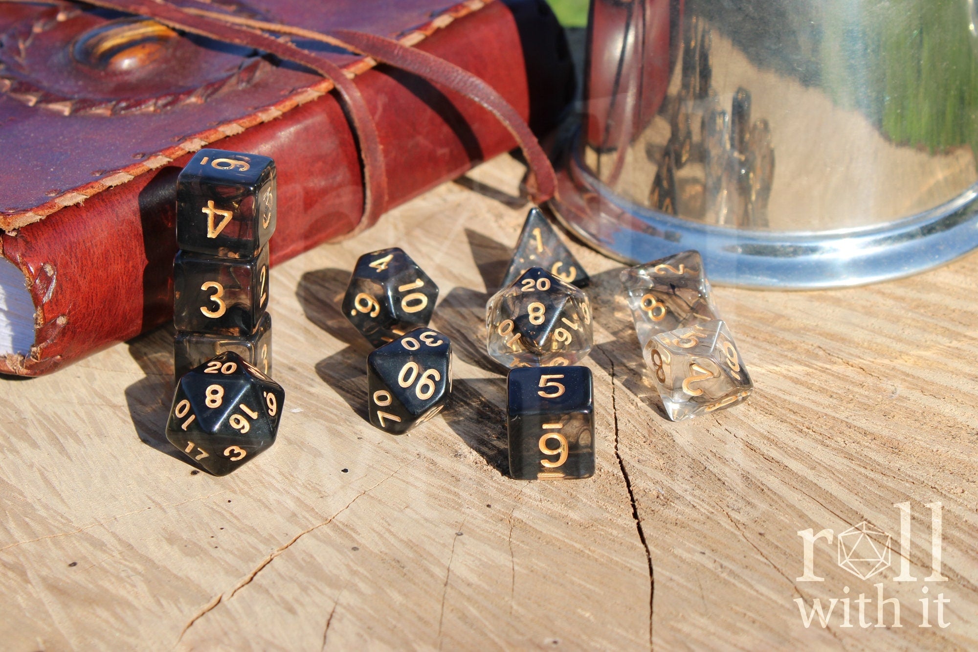 Set of 11 clear and smoky black polyhedral roleplaying dice on a wooden surface with tabletop RPG accessories in the background