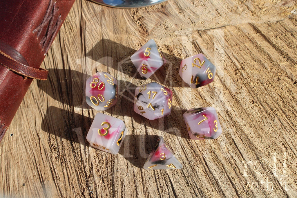 Set of black, red, and creamy white roleplaying dice with marbled design and gold numbers on a wooden surface