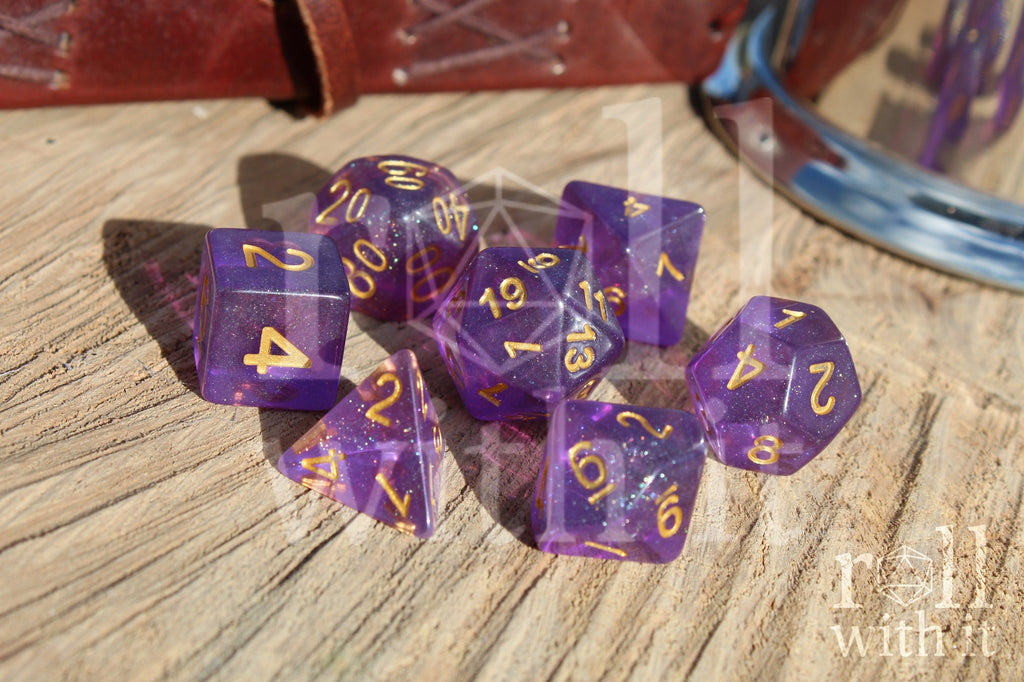 Set of glittery purple polyhedral dice with gold numbers on a wooden surface