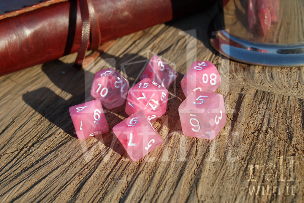 Set of cloudy pink and clear polyhedral roleplaying dice with white numbers on a wooden surface