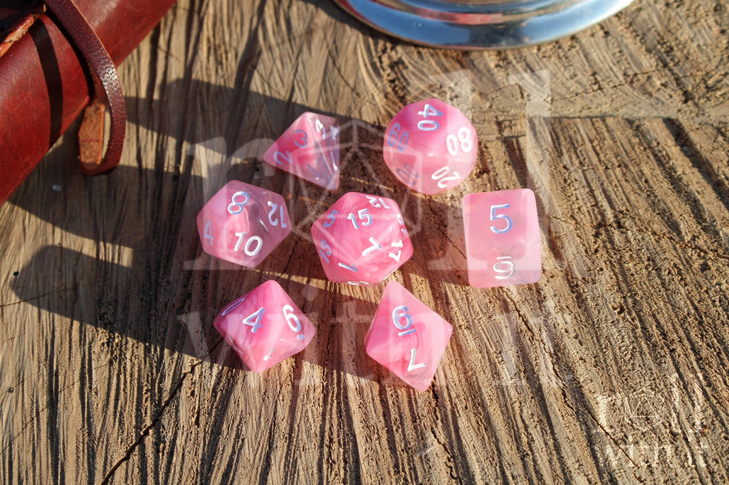 Set of cloudy pink and clear polyhedral DND roleplaying dice with white numbers on a wooden surface