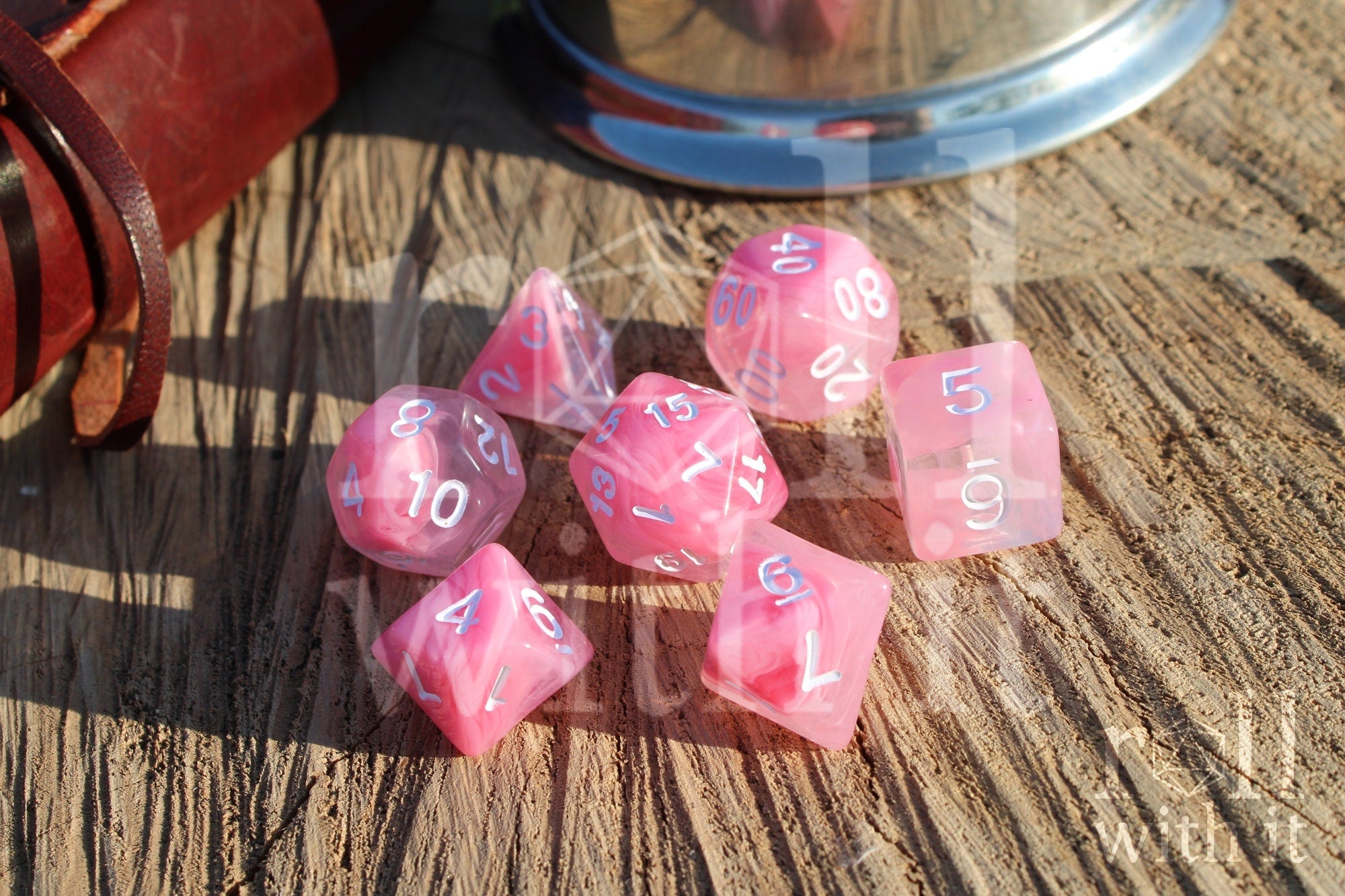 Set of cloudy pink and clear polyhedral RPG dice with white numbers on a wooden surface