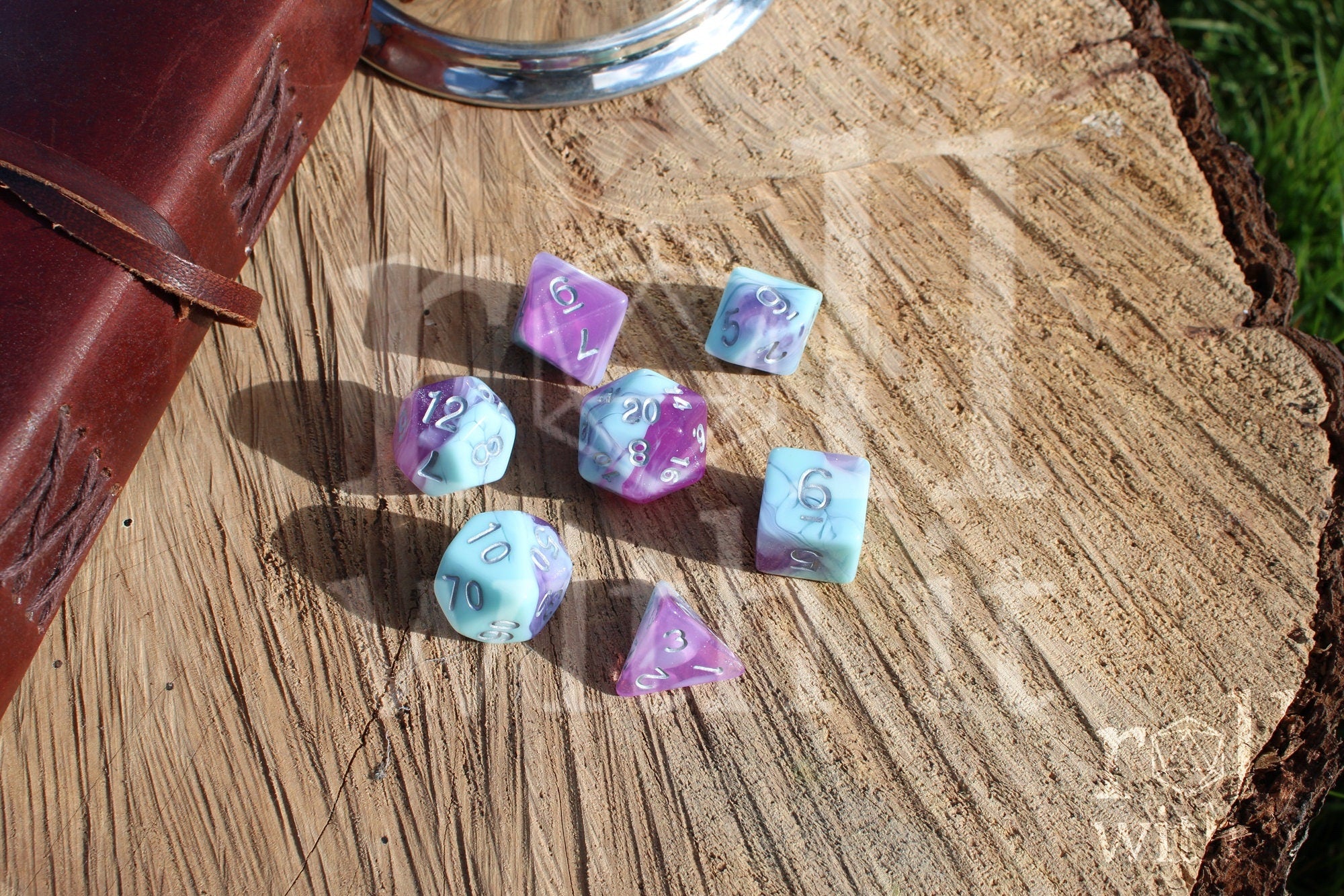 Set of 7 pastel blue marble and clear orchid purple polyhedral DND roleplaying dice on a wooden surface