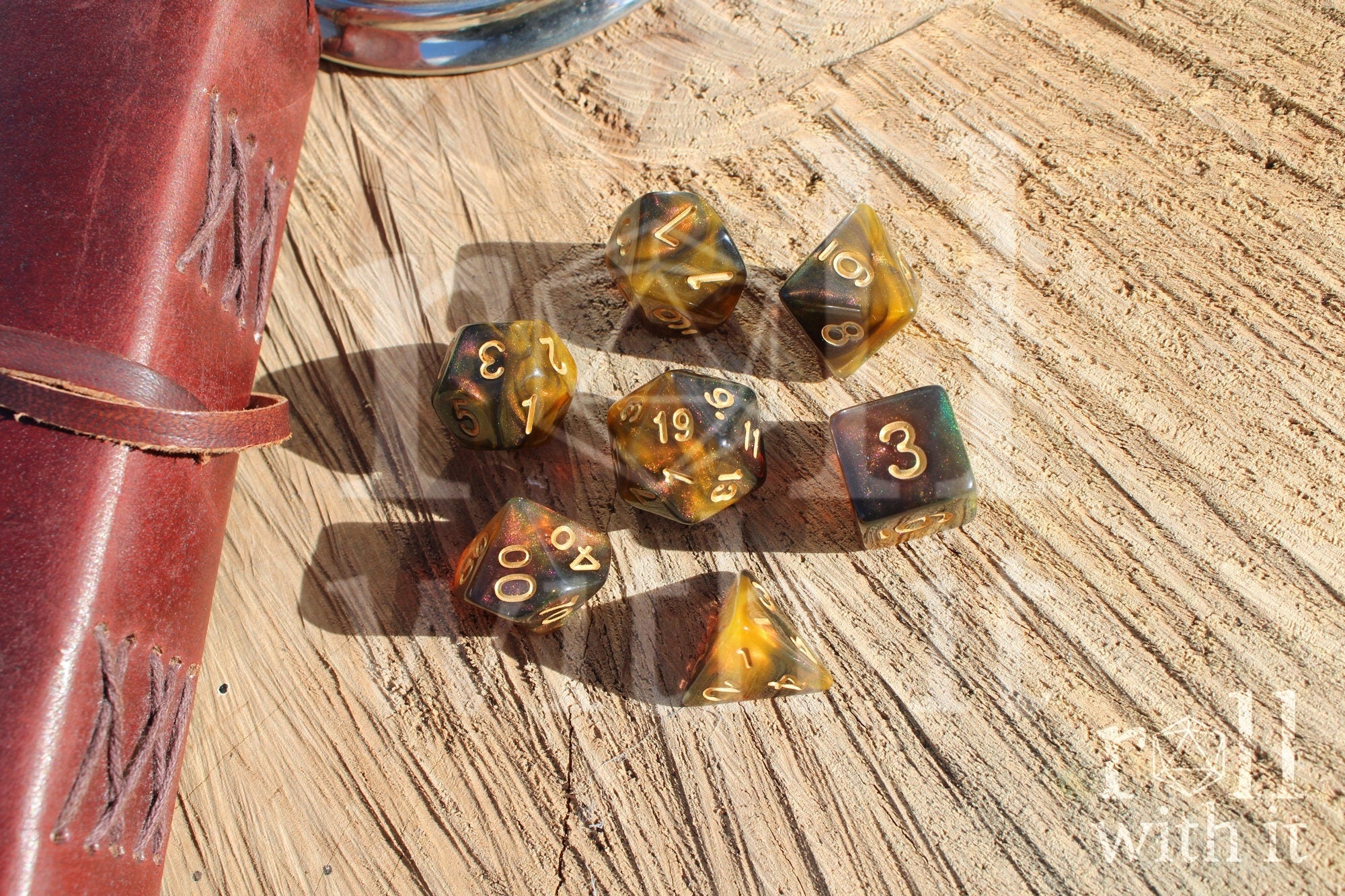 Set of 7 glittery green, smoky amber and orange swirling polyhedral roleplaying dice on a wooden surface.