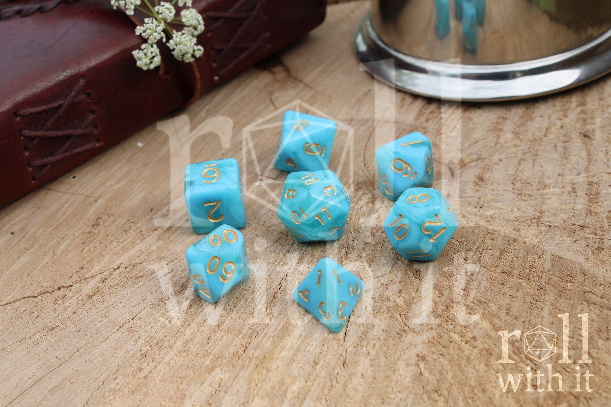 Set of light blue polyhedral roleplaying dice with gold numbers on a wooden surface.