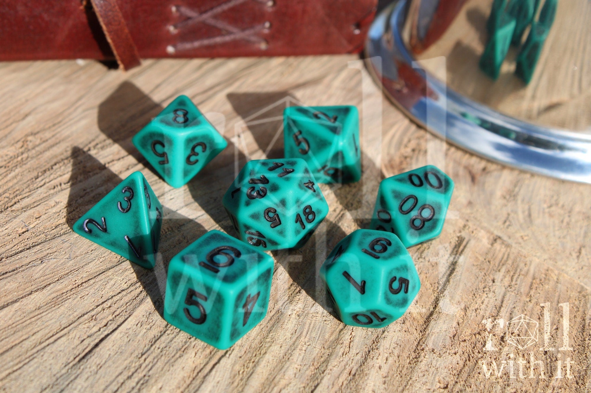 Matte teal polyhedral dice set with black letters on a wooden surface