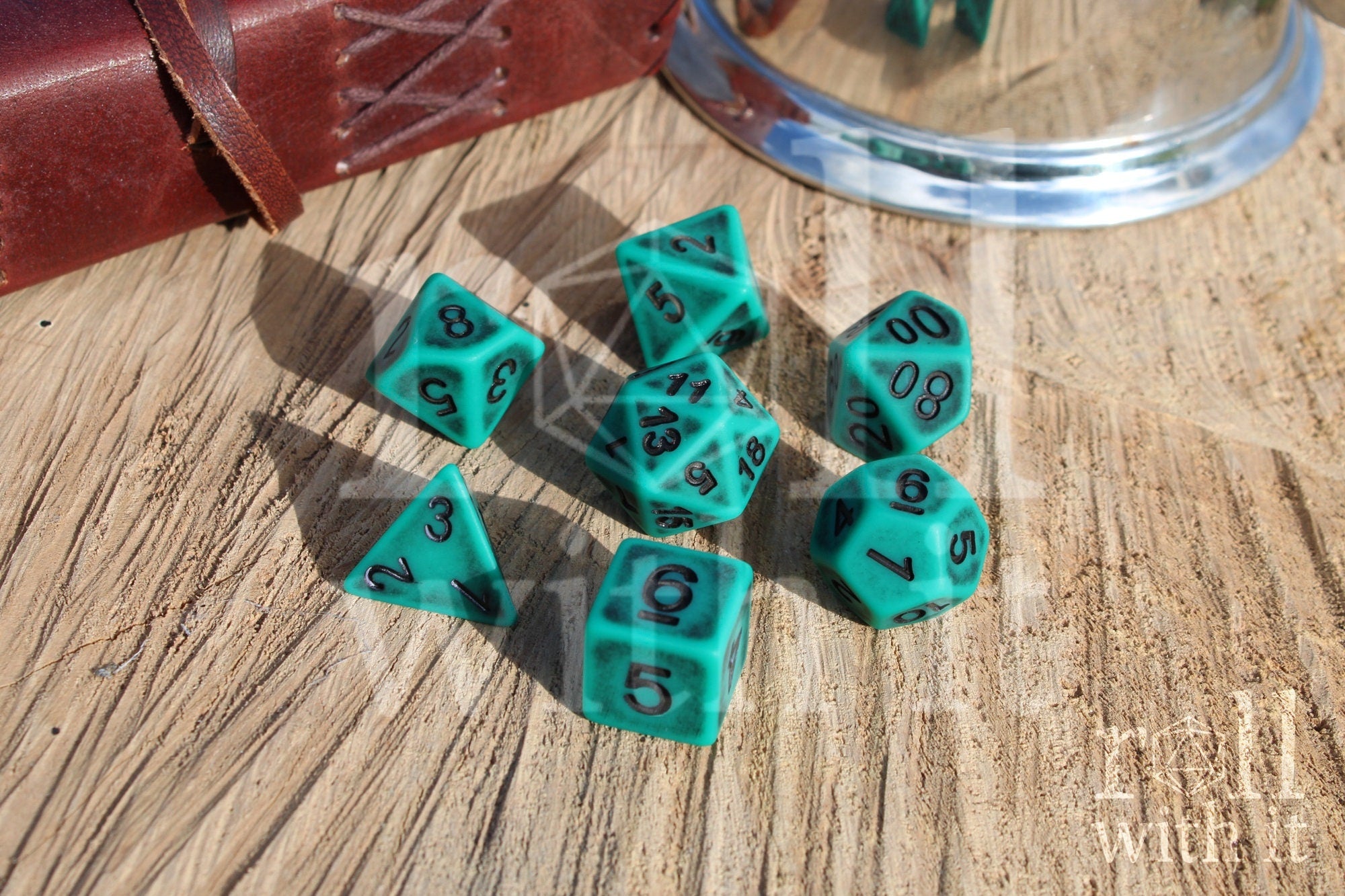 Matte teal polyhedral dice set with black letters on a wooden surface